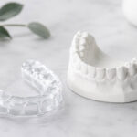 A custom dental nightguard beside a lower tooth model, illustrating how mouthguards help with TMJ