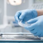A clinician's gloved hands adjusting a clear custom nightguard in a dental clinic.